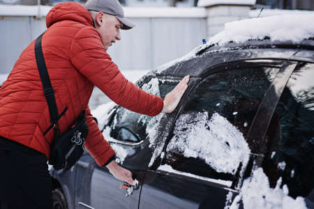 Frozen car door. Automobile car door or lock is frozen shut. Man driver trying to open frozen car door or lockの写真素材