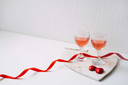 Valentines Day Festive table setting with two glasses of rose wine, red heart shape chocolate candies and red ribbons on white background. Valentine Day, romance, dating concept, copy spaceの写真素材