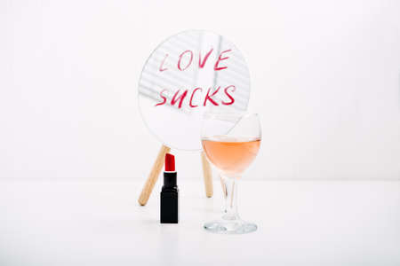 Loneliness, Broken heart, Divorce, couple breakup and relationship family breakdown concept with red lipstick text Love Sucks on mirror, glasses of rose wine on table.の写真素材