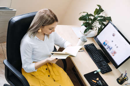 SMM specialist, Social Media Expert, Remote Social Media Pro. Young girl SMM manager with a phone at the workplace near computer with open social media page websiteの写真素材