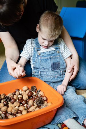 Sensory Play for Kids with Special Needs. Help and Activities for kids with disabilities, Cerebral Palsy. Boy with Cerebral Palsy playing with natural materials cones and nutsの写真素材