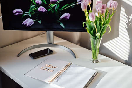 Self Care, wellbeing concept with open notebook, Self care word, tulip flowers, monitor and smartphone on white table at home. Take care of yourself, self care routineの写真素材