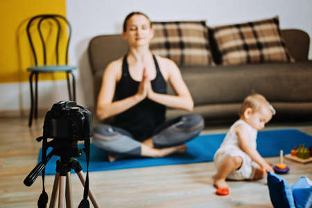 mother fitness instructor personal trainer record video near camera at home with baby daughterの写真素材