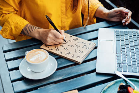 Woman freelancer writing numbers in notepad while working with laptop in street cafe. Time Managementの写真素材