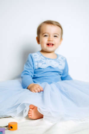 Cute baby girl in blue princess dress playing with toys at home. Kids dresses for prom and birthday holidayの写真素材