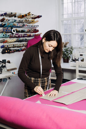 Female fashion designer tailor making sewing patterns at workplace in sewing studio.