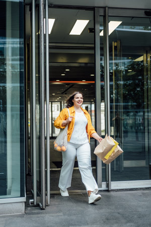 Happy confident smiling plus size curvy young woman with shopping bags walking on city street near...