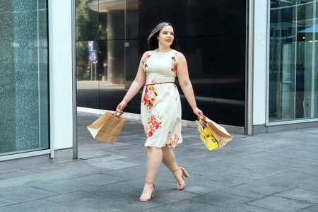 Happy confident smiling plus size curvy young woman with shopping bags walking on city street near...