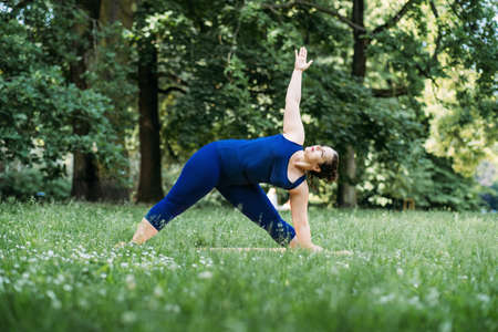 Happy confident smiling plus size curvy woman doing yoga stretching pilates workout, exercising outdoors.の写真素材