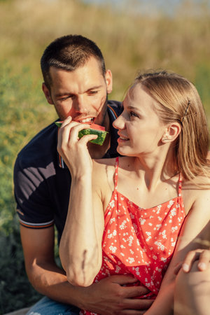 Happy loving couple kissing and having date outdoors. Young couple on summer picnic with watermelon.