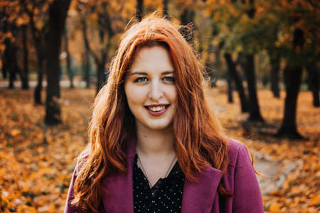 Autumn portrait of candid beautiful red-haired girl with fall leaves in hair.の写真素材