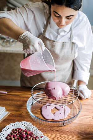 Mousse heart shape pink cake in hand of Asian Arabic woman pastry chef. Mirror Glaze Cake. Processの写真素材