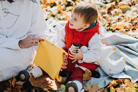Happy family mother and little toddler baby daughter having autumn picnic with red cup
