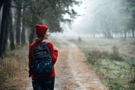 Weekend breaks and getaways in forests. Stay close to nature. Young woman in red hat and sweater with backpackの写真素材