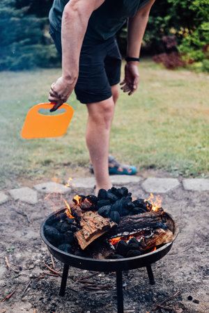 How to Use a Charcoal Grill. Man with Plastic BBQ Hand Fan near Charcoal Grill Fire. Barbeque Plastic BBQ Hand Fanの写真素材