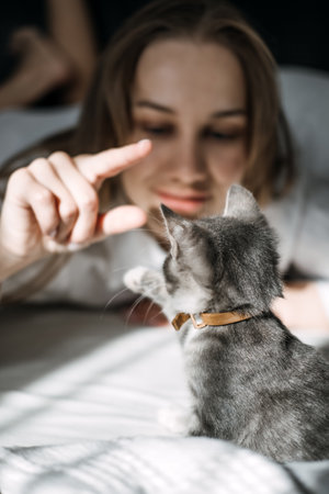 Candid portrait of young woman is resting with kitten pet on the bed at home one sunny day.の写真素材