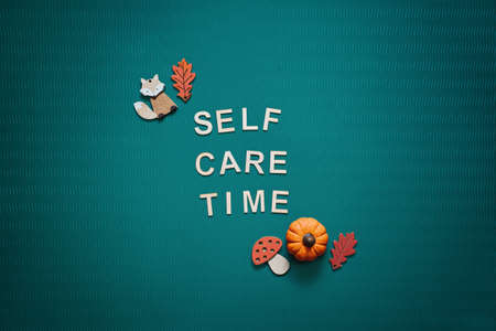 Self-care word on green background flat lay. Self-care text wooden letters with body face care products and autumn decorの写真素材