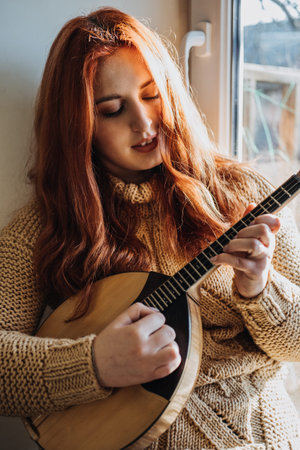 Redhead woman playing acoustic Domra Folk Musical Instrument and looking into note. Young woman...