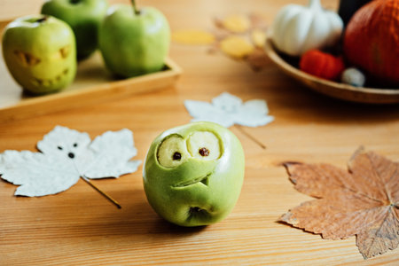 Halloween Fruit ideas. Halloween green apple with creepy carved face on wooden table at home....