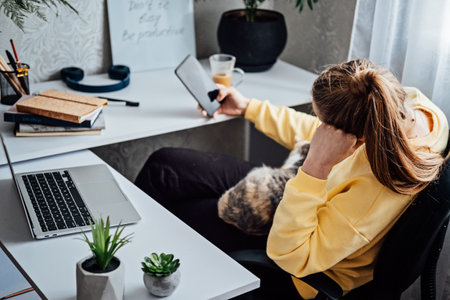 Woman freelance or procrastinate at workplace at home office. Self-employed businesswoman with cat distracted from work on laptop scrolling social media on smartphone.の写真素材
