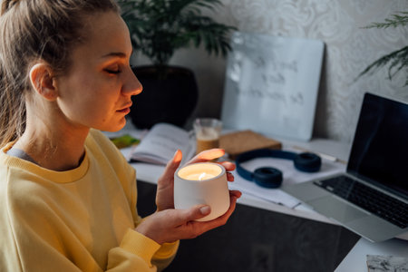 Young woman sitting on workplace at home office with lights candles, enjoy meditation, relaxing at home. Mental health, self care, No stress, mindfulness lifestyle, anxiety relief conceptの写真素材