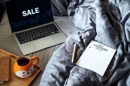Black Friday sale. Shopping List in note book near laptop with word Sale and tea coffee cup at bad...