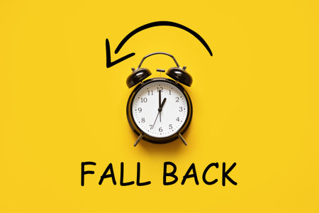 Daylight saving day. Fall Back. Black Alarm clock and autumn leaves and text Fall Back on yellow...