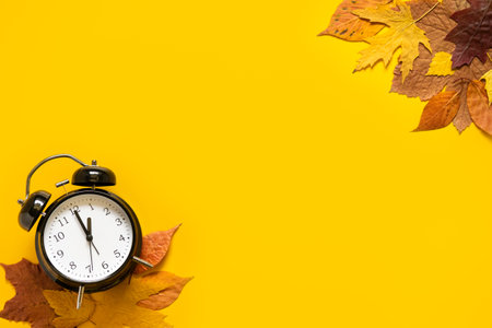 Daylight saving day. Fall Back. Black Alarm clock and autumn leaves on yellow background. Daylight saving time endの写真素材