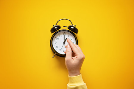 Daylight saving day. Fall Back. Black Alarm clock and female hands on yellow background. Daylight...
