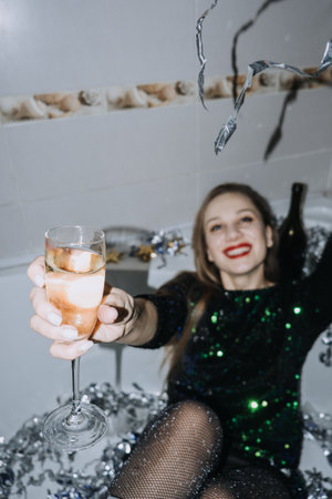 New Years Party celebration. Happy young woman in evening dress sitting in the bathtub drinking champagne and having funの写真素材