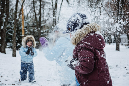 Happy Family, friends, mother and kids having fun outdoors in winter snowy nature background. Mom and two boys playing snowball at winter park outside. Outdoors winter activities for family, friends.の写真素材