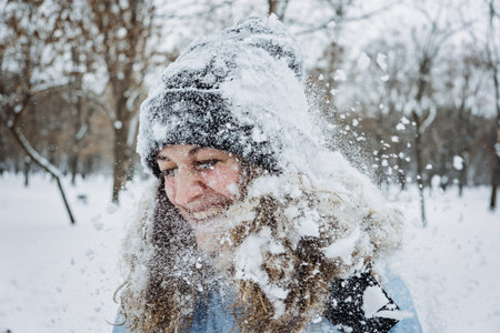 Close up outdoor winter portrait of woman in winter clothes. Candid portrait of young woman in winter time. Mom playing snowballs, walking under snow. Outdoors winter activities for adults, family.の写真素材