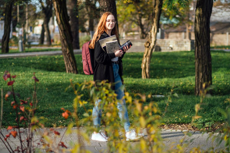 Choosing a university, college. Female college student with books and laptop outdoors. Redhead...