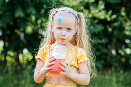 Outdoor portrait of Funny grimy little girl with two ponytails drinks lemonade sweet sweetened drinks, fizzy on summer day. Sugar in Kids Drinksの写真素材