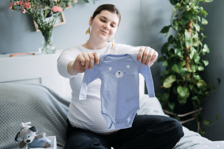 Pregnant woman with big belly holding bodysuit and sorting clothes for future. How to Organize Newborn Baby Clothes. Preparing things in pregnancy time.の写真素材