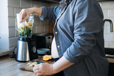 Smoothies and food for Pregnancy Nausea. Anti-nausea morning sickness smoothie. Pregnant woman preparing green vitamin smoothie from variety of fruits and vegetables with a blender in kitchenの写真素材