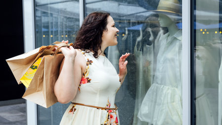 How to Shop for Summer Fashion on a Budget. Choosing the Right Fabrics for Hot and Humid Summer Weather. Outdoor portrait of stylish curvy woman with shopping bagsの写真素材