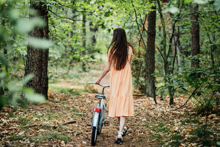 Walk in the woods for wellness, Health benefits of forests. Immerse Yourself in a Forest. A young girl rolls a bicycle along a forest path in tree woodの写真素材