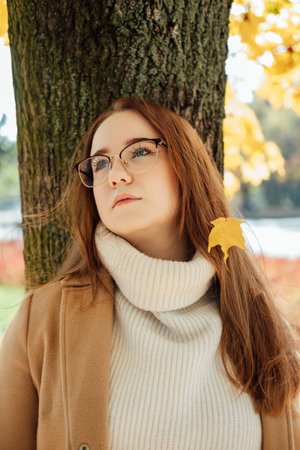 Autumn wellbeing, protect mental health concept. How to Cope With Fall Anxiety. Beautiful black woman. Portrait of beautiful redhead student woman in glasses on fall autumn tree backgroundの写真素材