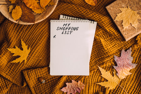 Black Friday, autumn fall season sale, autumn shopping. Shopping List in notebook notepad with autumn leaves, tea coffee cup at brown background in home. Shopping Preparation Consumer Buyingの写真素材