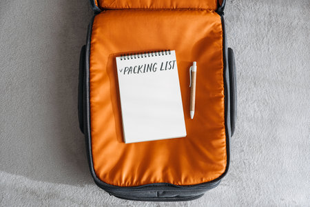 Travel Packing List For Vacation. Travel Packing Checklist For Holiday Or Business Trip. Open notepad with handwritten text Packing list in orange suitcase on bed at homeの写真素材