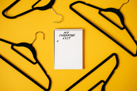 Black Friday Sale concept with black Clothes Hanger and notepad with text Shopping list on yellow. Store, sale, save money, shopping planning concept, empty hanger.の写真素材