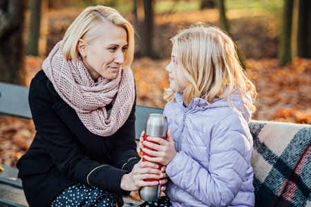 Creative Kid-Friendly Picnic Ideas For Autumn. Happy mother with teenager daughter with blanket and thermos on fall picnic. Mom and daughter picnic in the autumn parkの写真素材