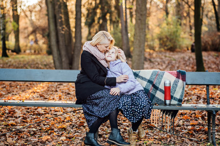Creative Kid-Friendly Picnic Ideas For Autumn. Happy mother with teenager daughter with blanket and thermos on fall picnic. Mom and daughter picnic in the autumn parkの写真素材