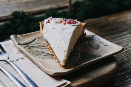 Creamy Cheesecake Slice on Botanical Ceramic Plate. Elegant cheesecake slice topped with dried petals, perfectly presented on a leaf-patterned ceramic plate.の写真素材