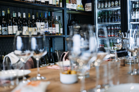 Wine Tasting Setup with Array of Bottles. Foreground of empty wine glasses set for tasting with a background of various wine bottles on shelves. Warsaw, Poland - May 02, 2023のeditorial素材