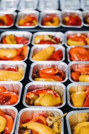 Pre-portioned Gourmet Roasted Bell Peppers in Trays. Close-up view of vibrant roasted bell peppers portioned in aluminum trays, prepared for a catered event or meal service.の写真素材