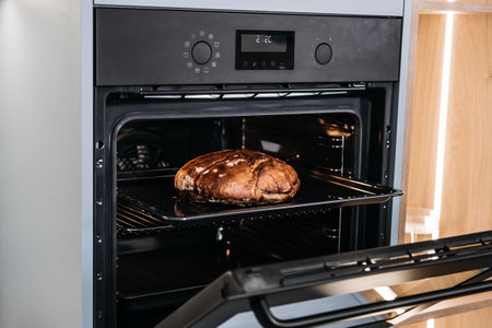 Freshly Baked Loaf of Bread in Modern Oven. Homemade baked artisanal loaf of bread sitting on the rack of a modern kitchen oven, exuding warmth and homeliness.の写真素材