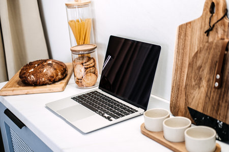 Kitchen Workstation Mockup with Empty Laptop Screen. An elegant kitchen setup with laptop empty screen ready for mockups, surrounded by tasteful home decor and natural light.の写真素材