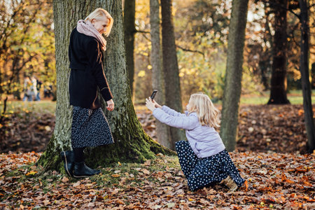 Parent-child bonds and mother daughter relationships. Mother and daughter embracing, capturing a special moment selfie together amidst the golden hues of autumn.の写真素材
